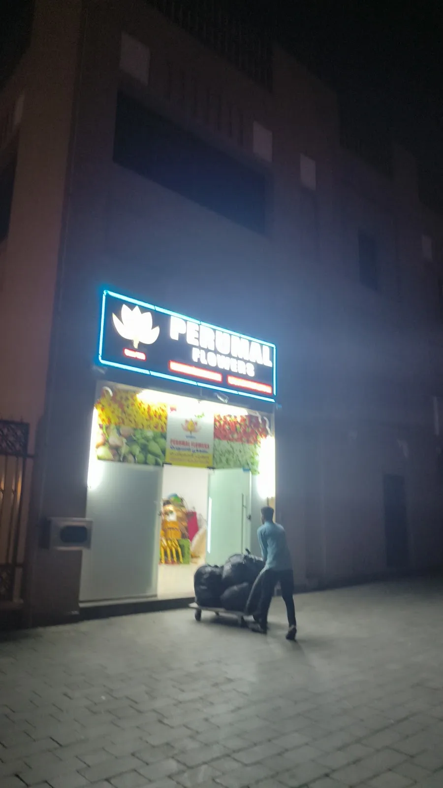 The Perumal Flowers shopfront glowing at night under a blue neon lotus sign.