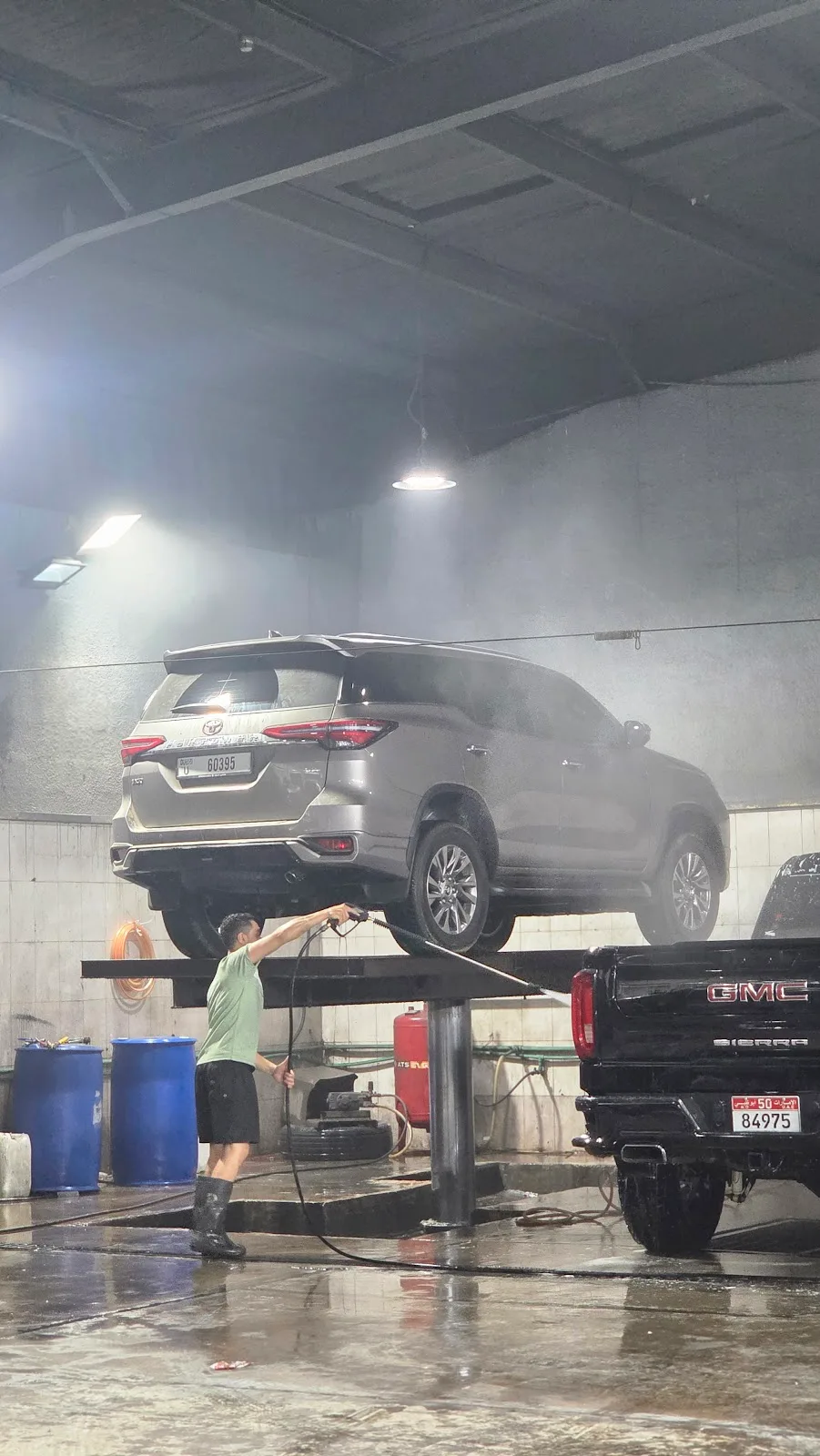 An SUV raised on a lift being steam-washed in the workshop