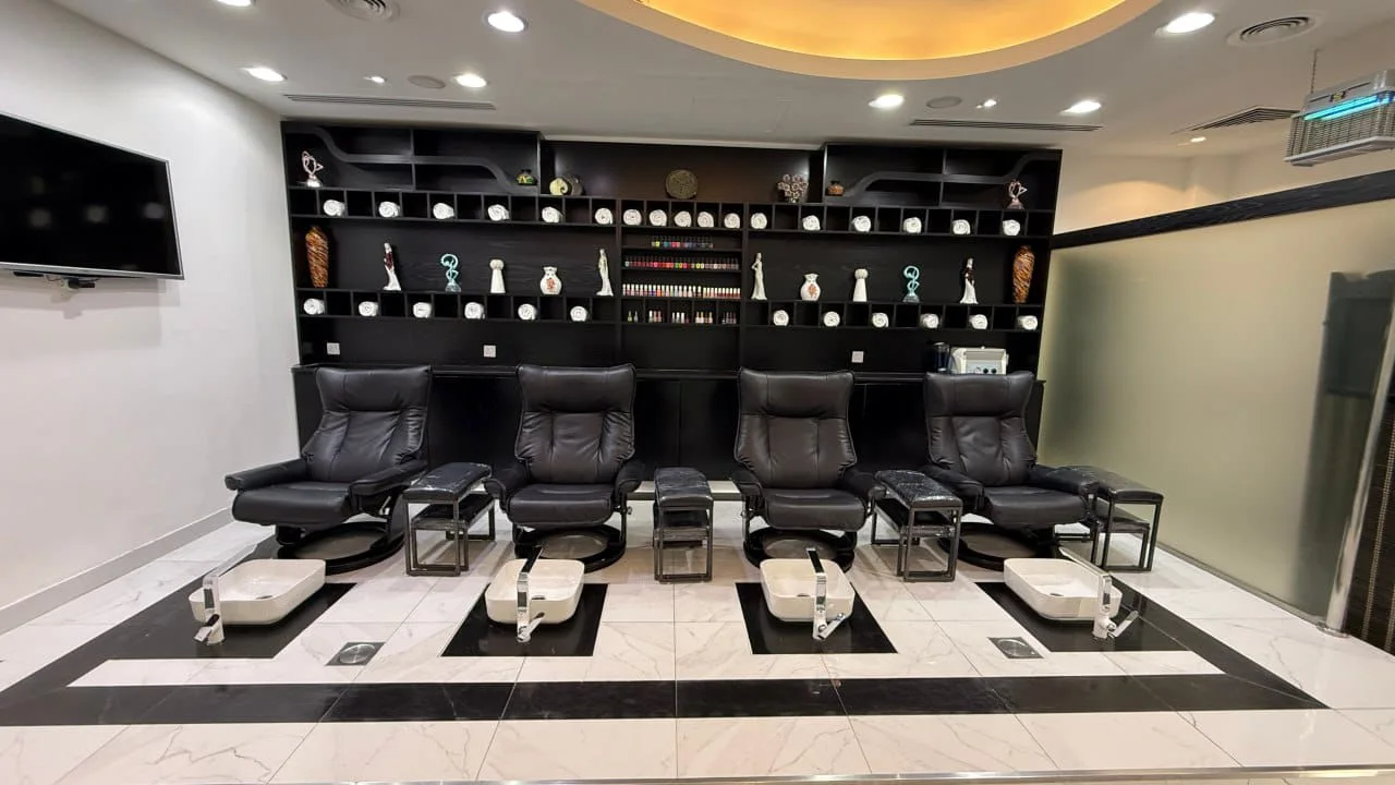 The pedicure lounge at Al Marfa Star Ladies Salon — black recliner chairs against a black display wall over a black-and-white marble floor