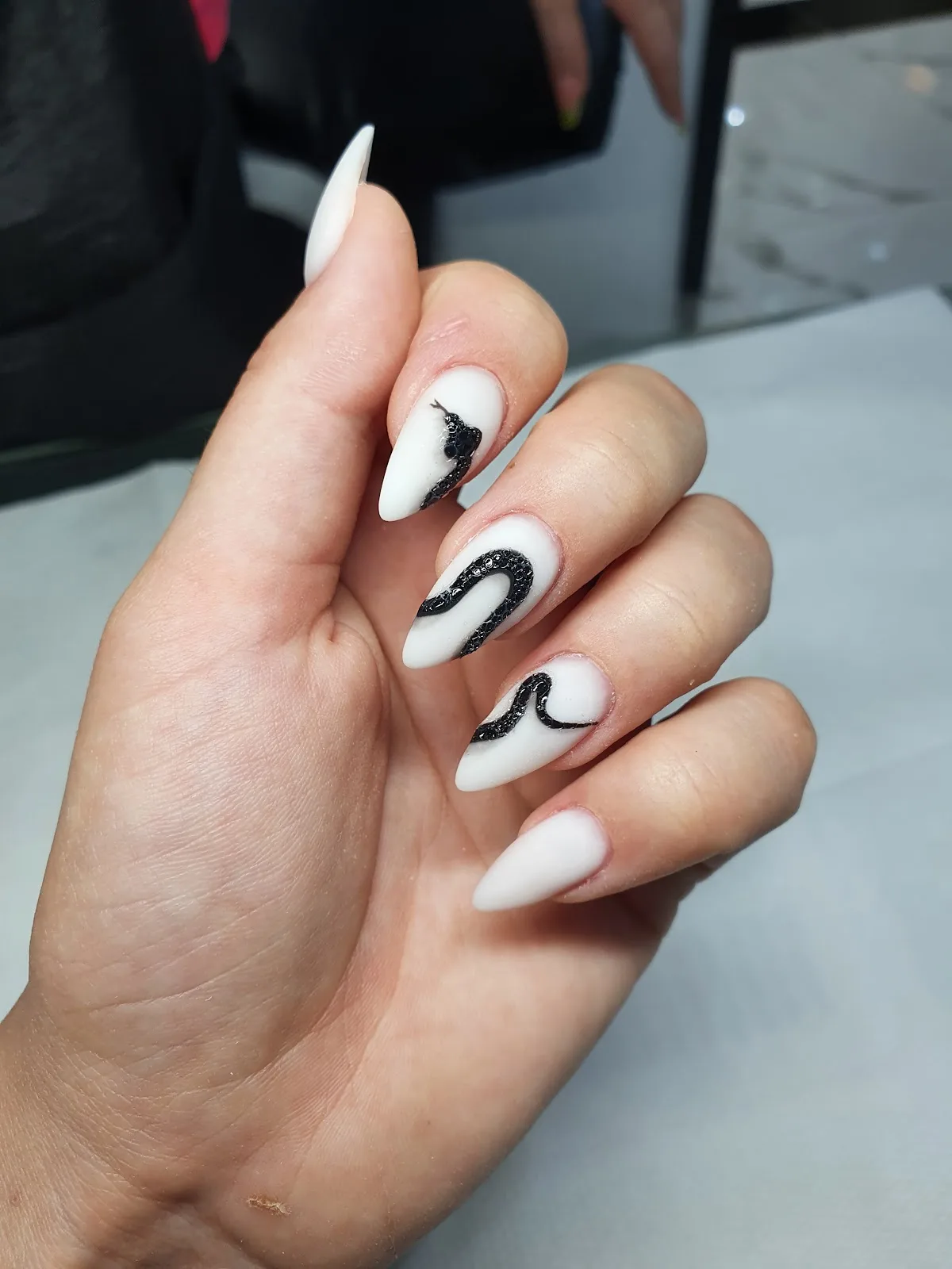 Matte white almond nails with black serpent nail art