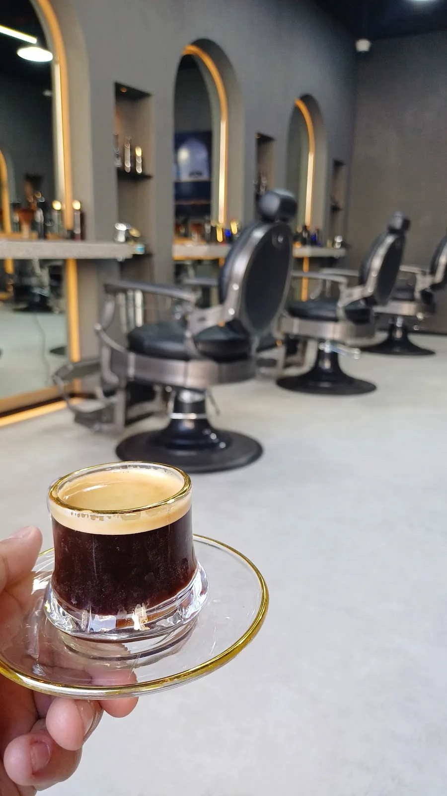 Small cup of Turkish coffee held in front of Diveno's barber chairs