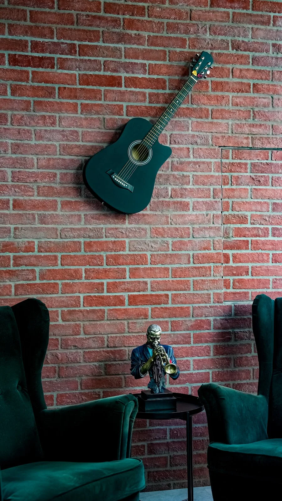 Acoustic guitar and a brass jazz-trumpet figurine on the salon's exposed brick lounge wall