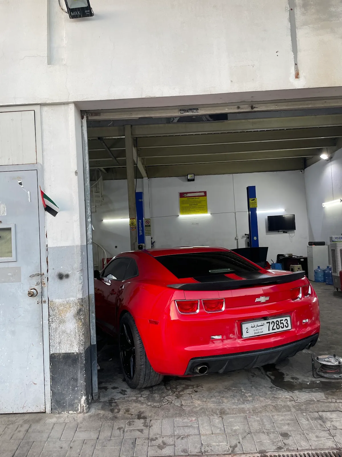 A red Chevrolet Camaro parked inside an open service bay at Bindarwash Garage in Umm Ramool, Dubai