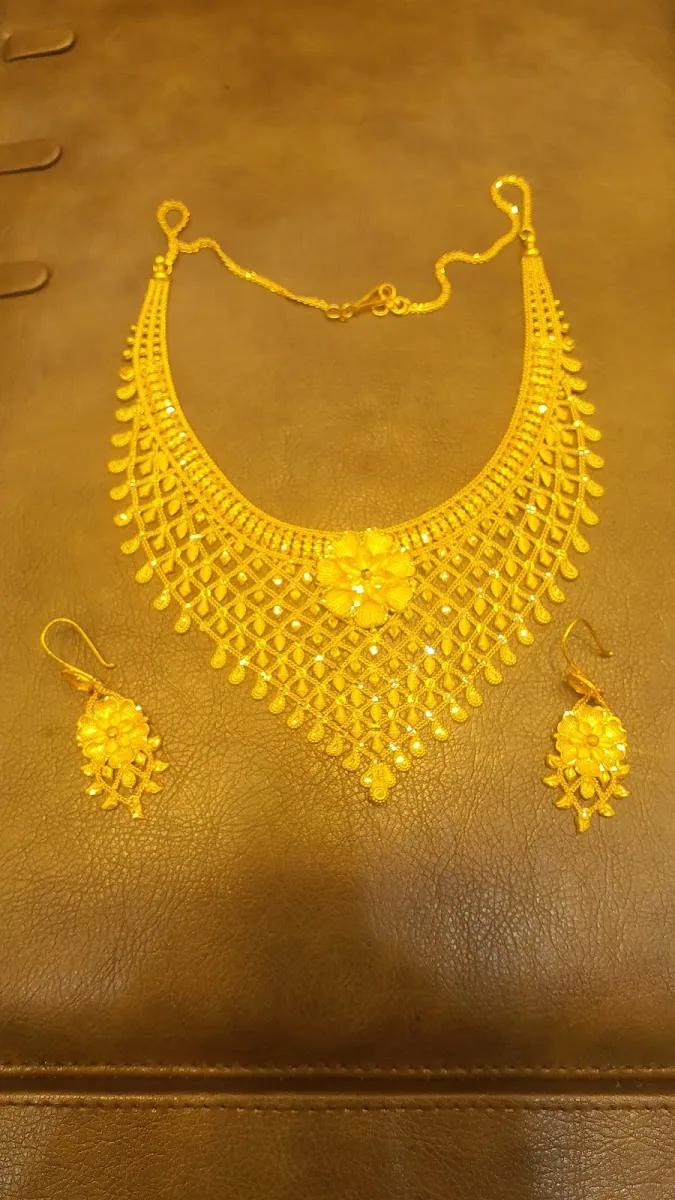 Delicate gold mesh necklace and matching earrings on a tan leather pad