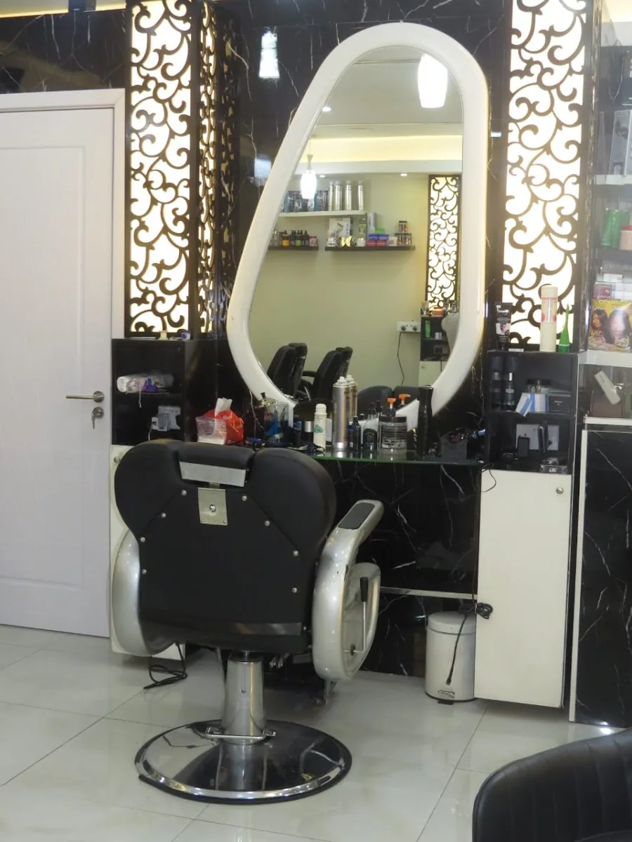 Chrome barber chair beside a backlit white filigree screen and tall mirror at Syriana Men Salon