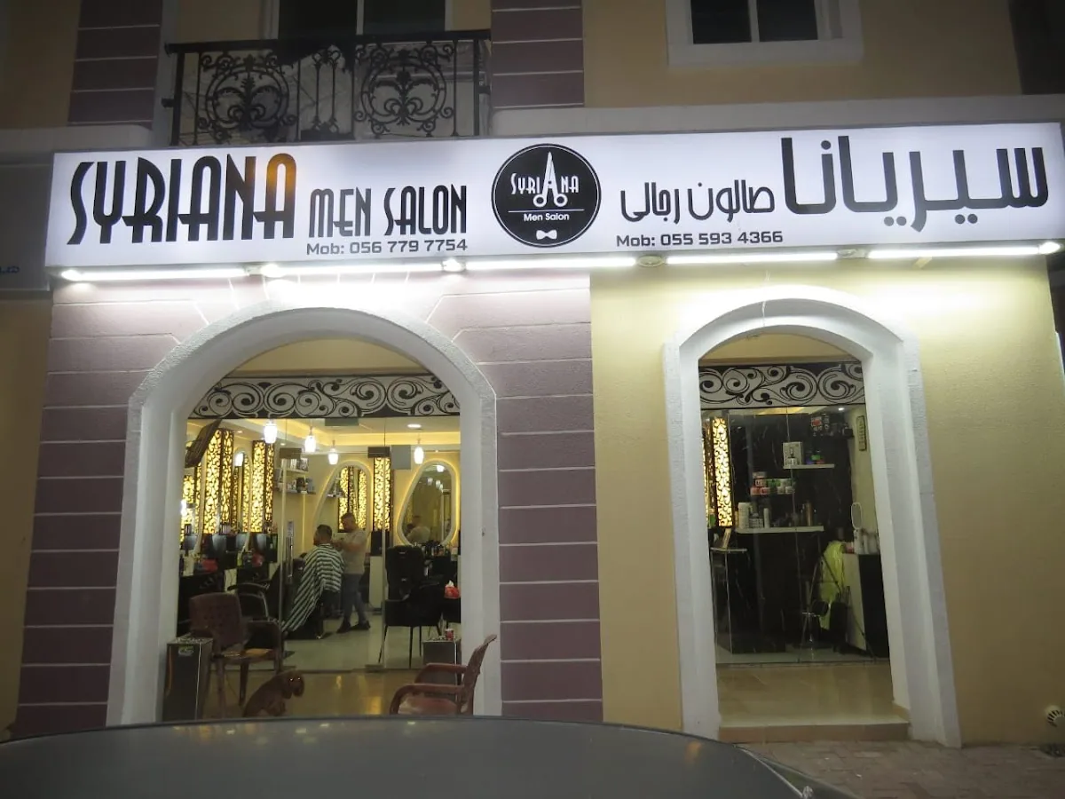 Syriana Men Salon storefront lit at night with its signage and arched entrances