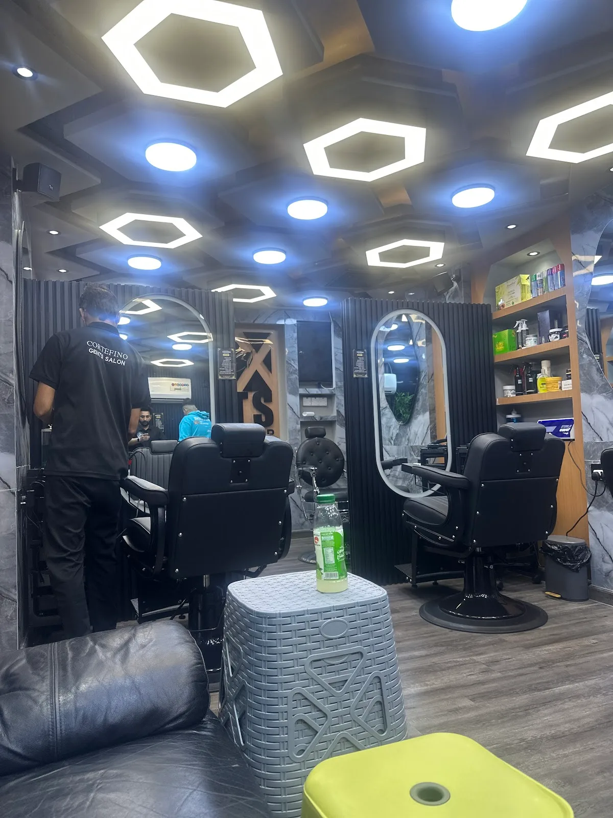 Barber chairs and an arched mirror under hexagon ceiling lights inside CorteFino Gents Salon