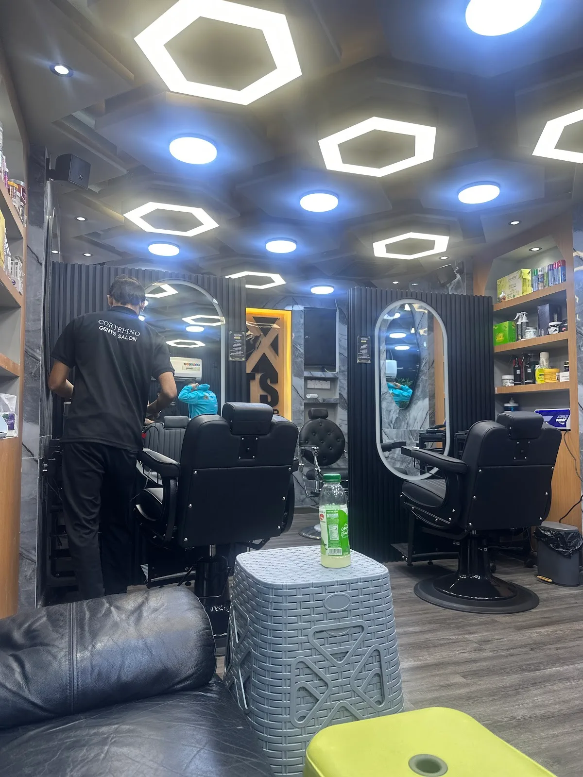 A barber at work beside marble walls and barber chairs inside CorteFino Gents Salon