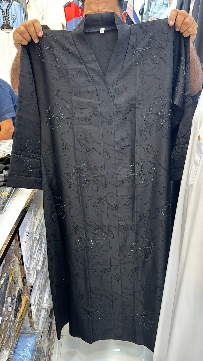 A black abaya with hand-applied floral beadwork held up at Top Naif Abaya Trading in Naif, Dubai