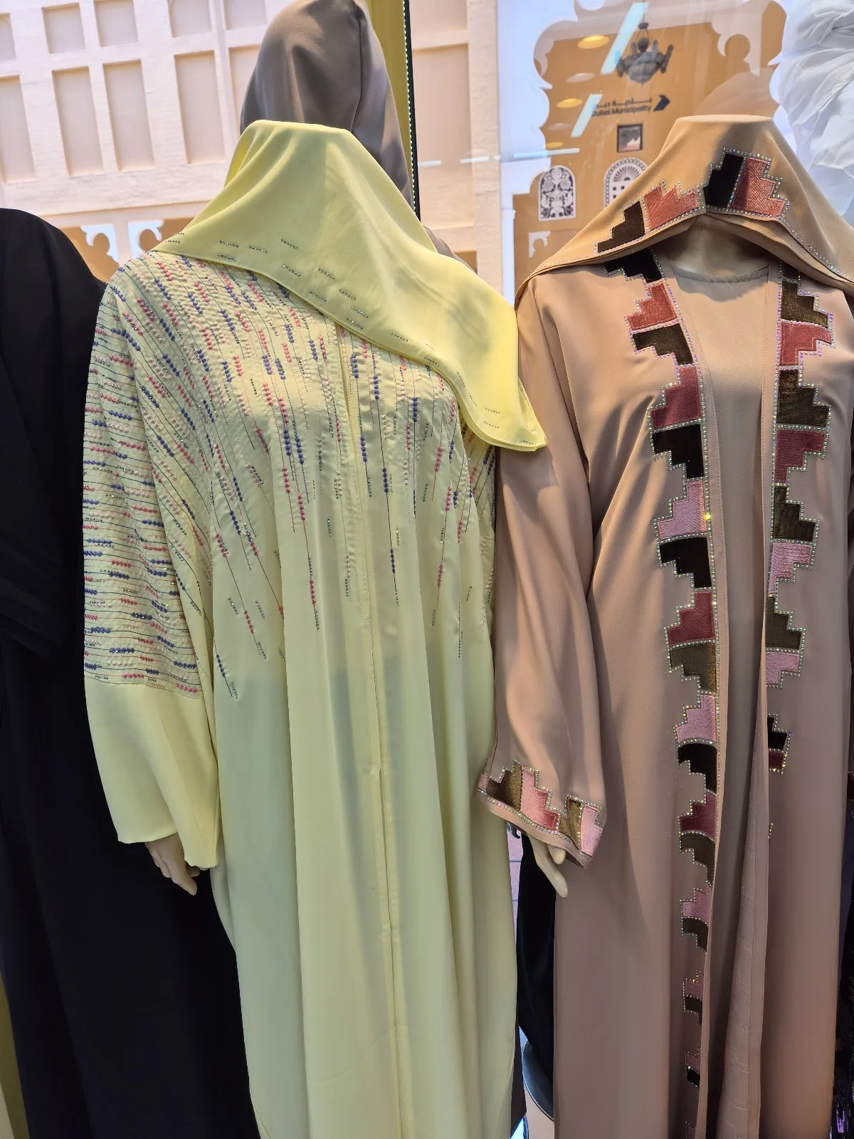 Two abayas in soft tones with geometric appliqué trim