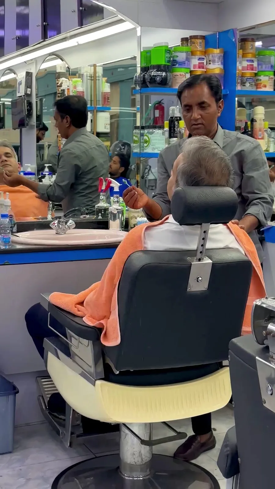 A barber at Yathreeb attending to a seated client at the mirror counter