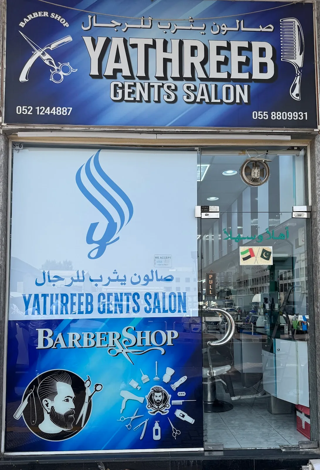 Yathreeb Gents Salon shopfront by day, showing the wordmark and barbershop graphic on the glass door