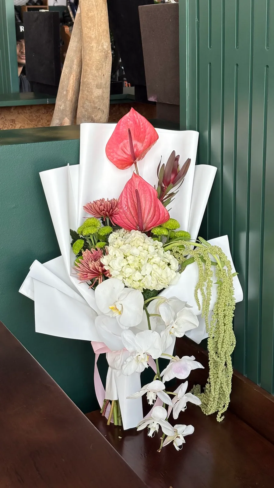 Hand-tied white bouquet with anthurium, orchids and hydrangea wrapped in white paper at Rowdat Al Zuhoor