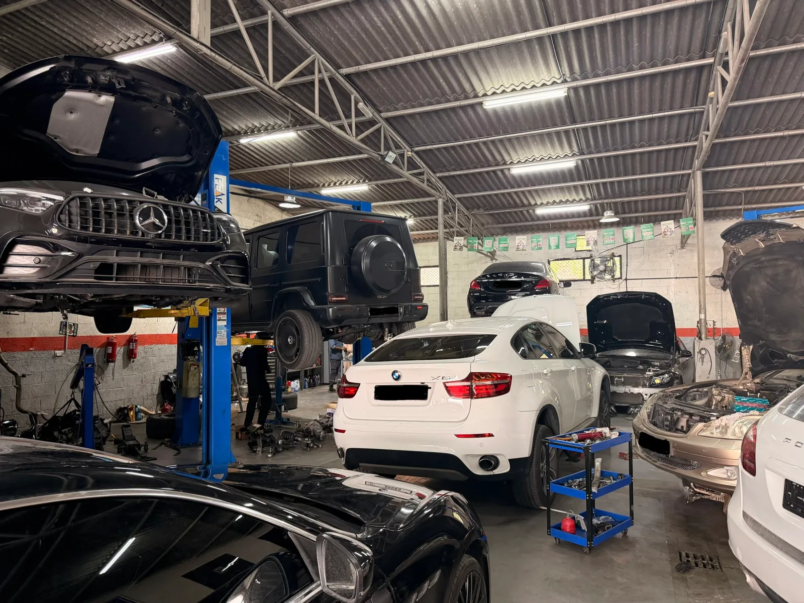 Cars on lifts inside the Muhammad Asghar Garage service bay in Umm Ramool, including a Mercedes G-Class and BMW X6