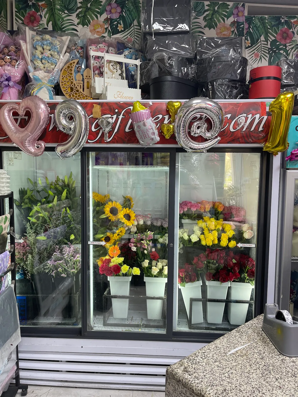 A florist display fridge filled with sunflowers, roses and seasonal flowers in buckets