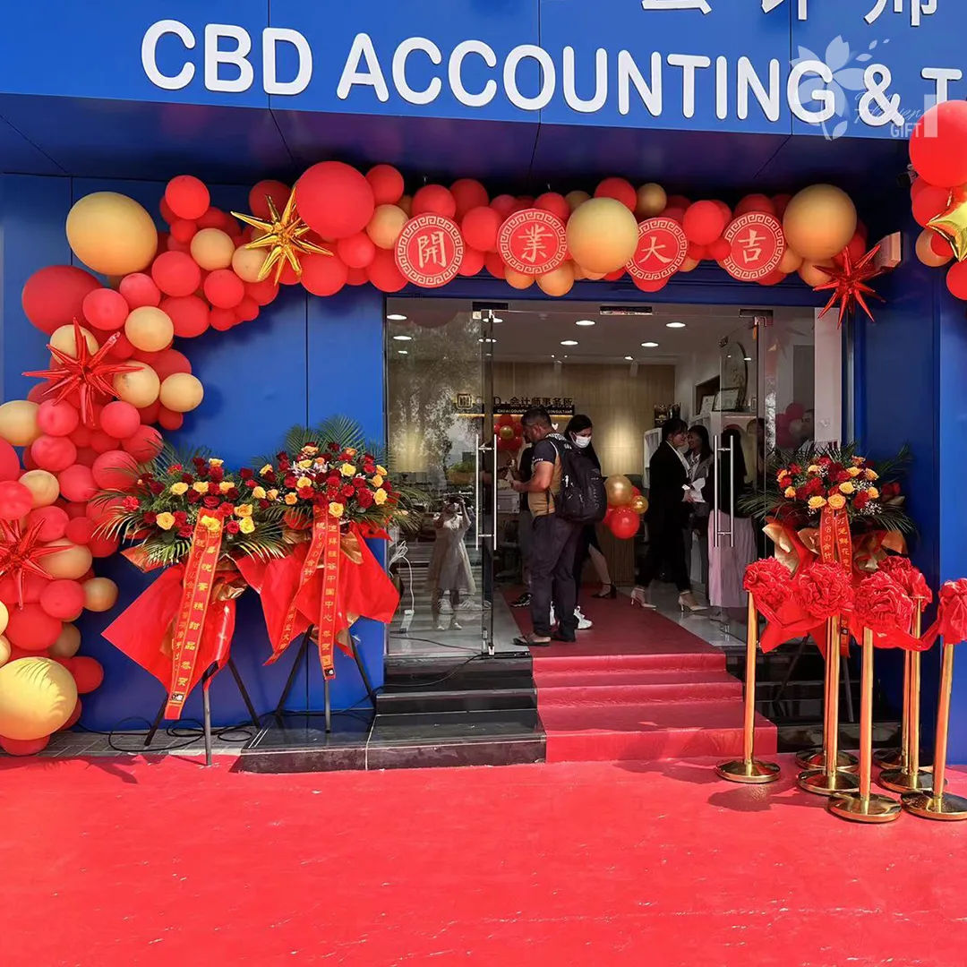 A red and gold balloon arch with congratulation flower stands at a shop grand opening