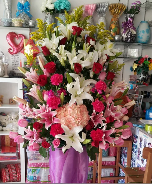 A tall arrangement of white lilies, red roses and pink carnations in a wrapped vase