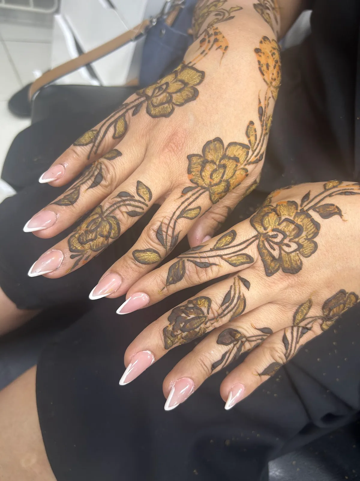 Gold and black floral henna with a French-tip manicure on a guest's hands