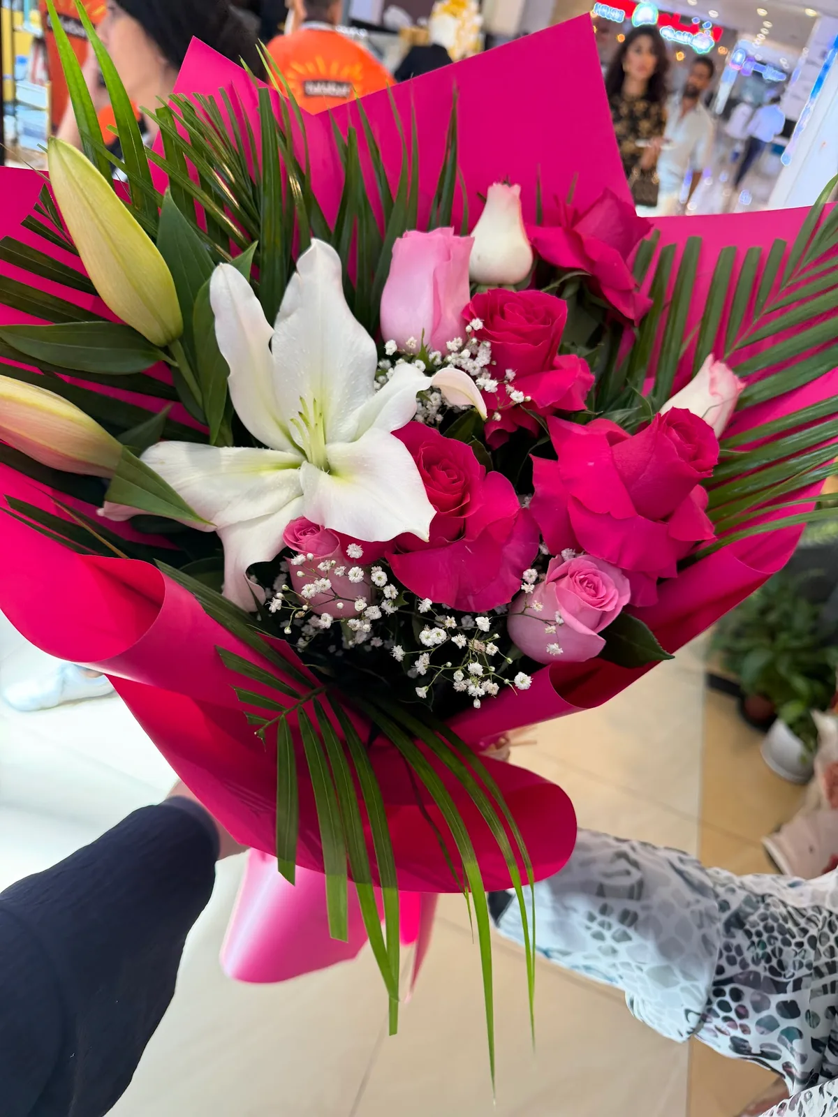 Hand-tied bouquet of pink roses and a white lily wrapped in magenta paper