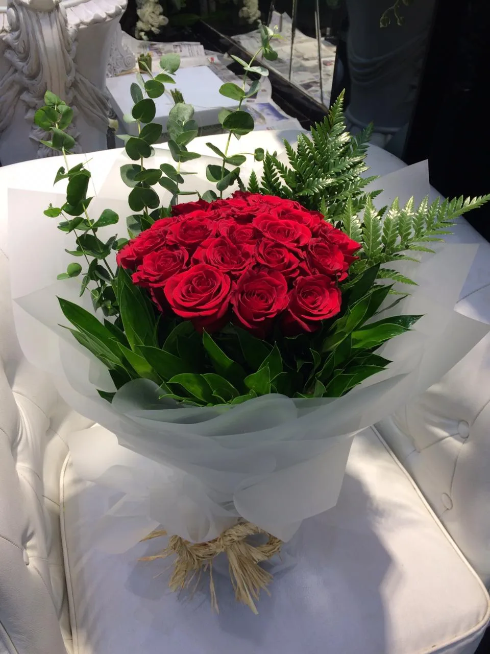 A neat bouquet of red roses wrapped in soft white paper with eucalyptus and ferns
