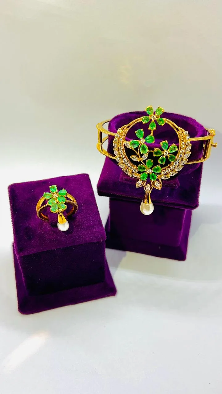 Gold bangle and ring set with green floral gemstone clusters and a pearl drop, on purple velvet boxes