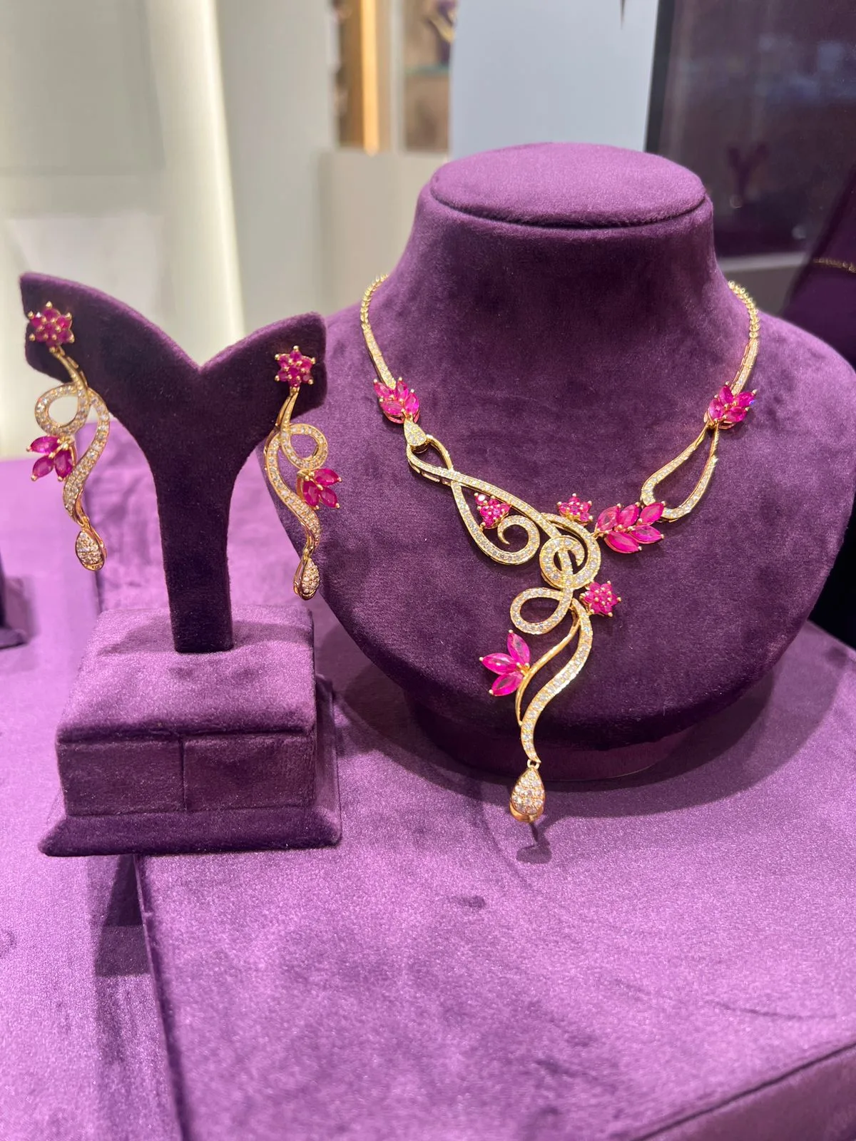 Gold necklace and earring set with marquise-cut ruby-pink and white stones on a deep purple velvet display at Al Saif Jewellers