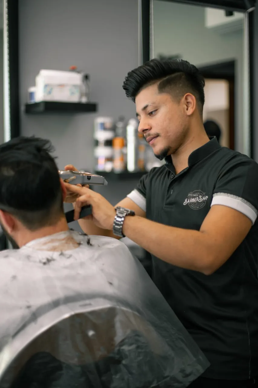 Kingsmen barber in a branded polo trimming a client with clippers