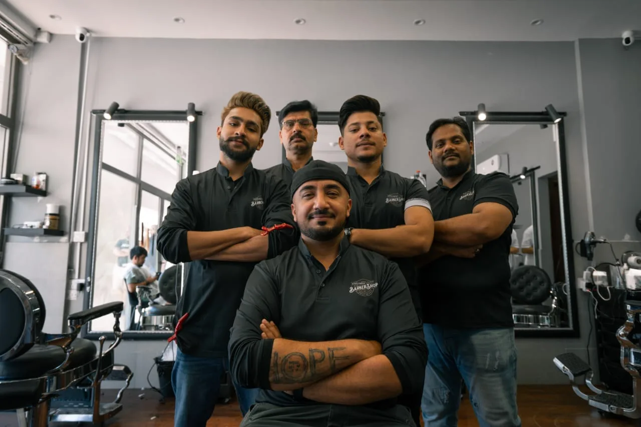 The Kingsmen Barbershop team in branded black shirts inside the shop