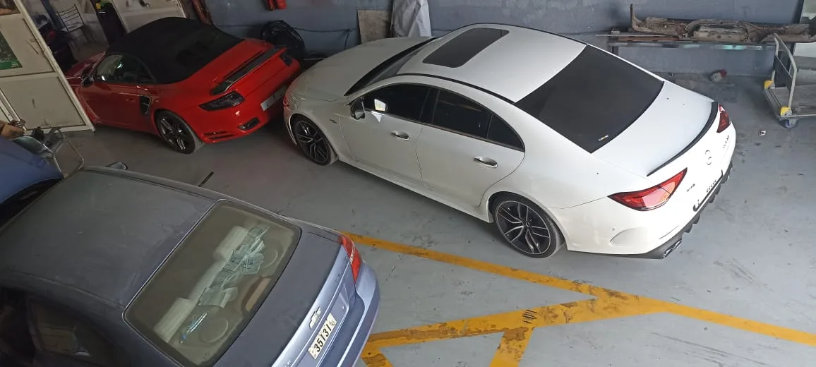 A white Mercedes-AMG and a red Porsche 911 parked inside the workshop bay, seen from above.