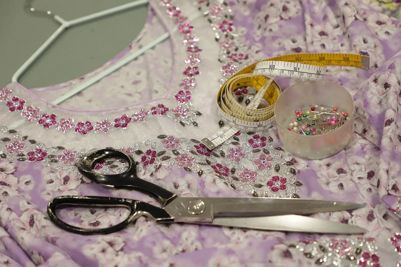 Lilac floral dress with pink and silver embroidery, tailor's scissors and a measuring tape