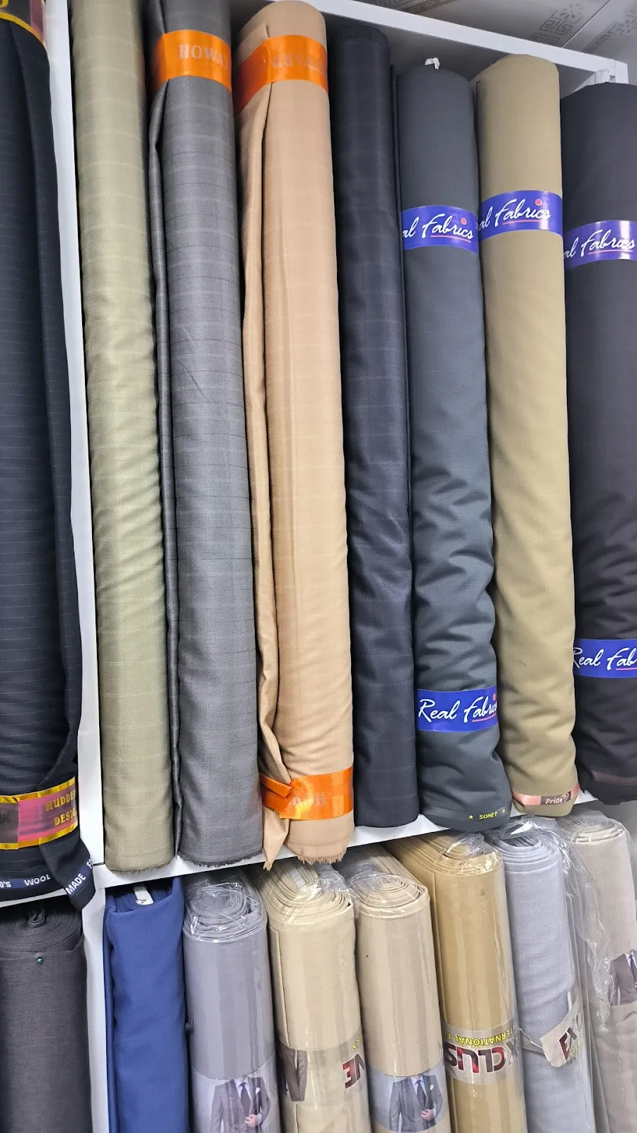 Rolls of grey, beige and navy suiting fabric stacked on the shelf at Qasar Al Ajaz