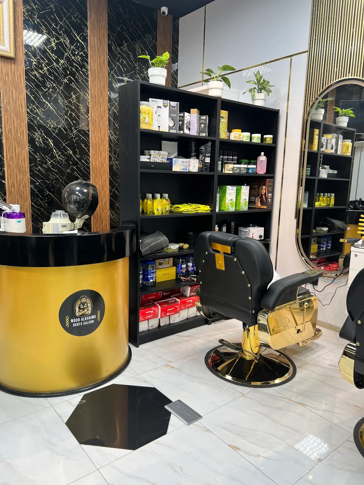 Gold reception counter at Noor Al Khaima Gents Salon with the salon emblem, beside a black-and-gold barber chair and product shelves