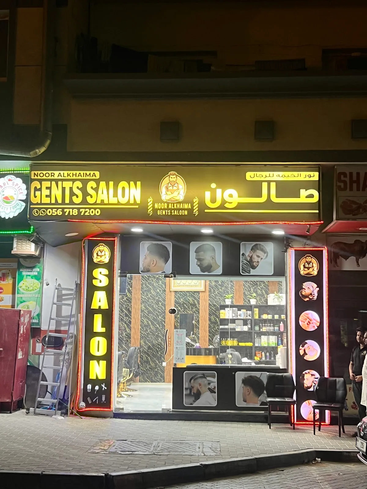 Noor Al Khaima Gents Salon storefront lit up at night on 1B Street, Hor Al Anz, with its gold sign and barber-style window photos