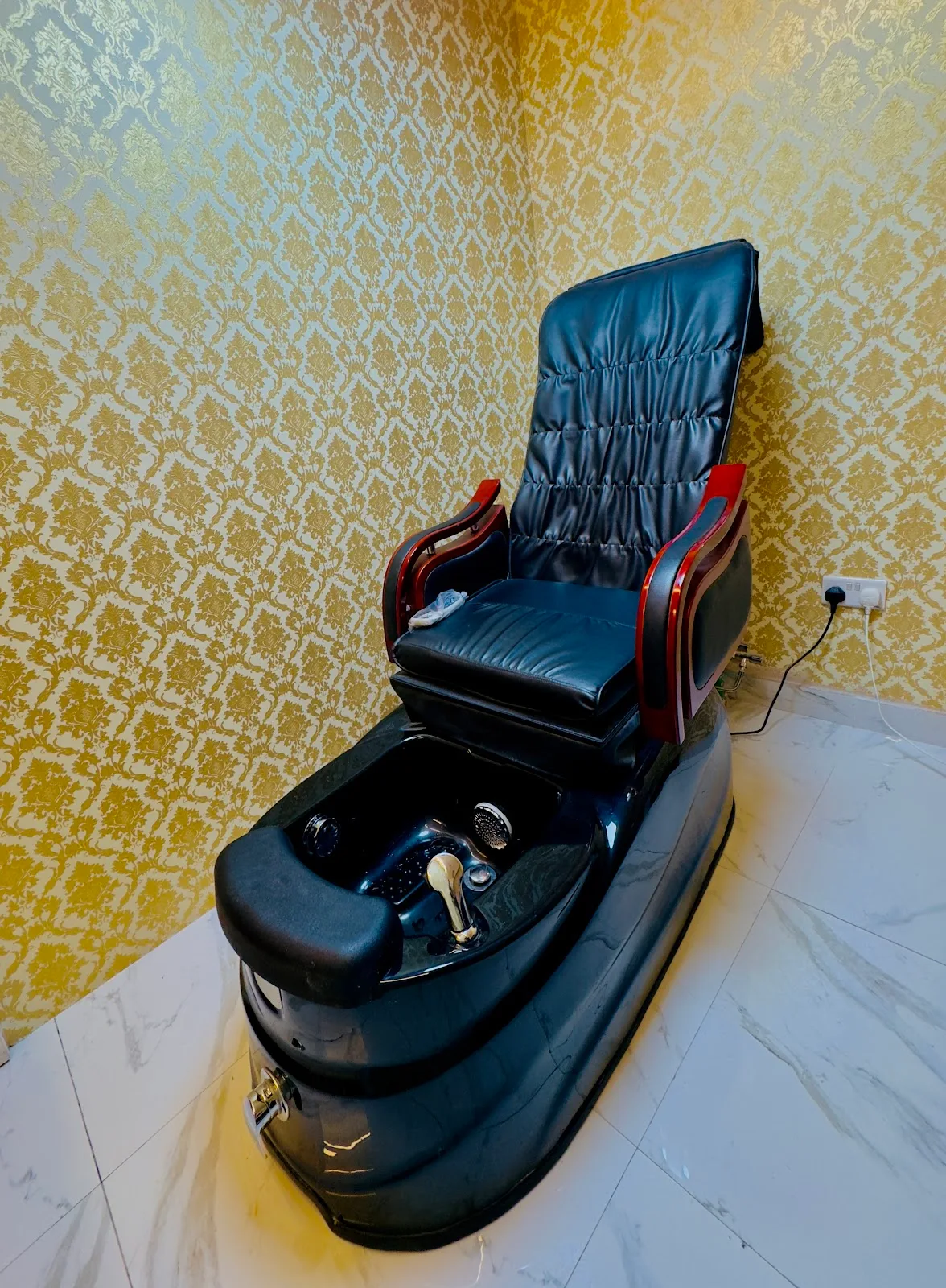 Black leather foot-spa and pedicure chair set against gold patterned wallpaper