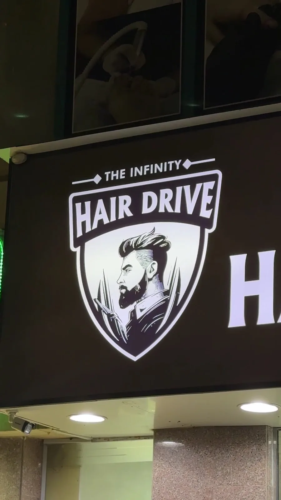 THE INFINITY HAIR DRIVE shield logo — a bearded gentleman in profile — illuminated on the salon sign