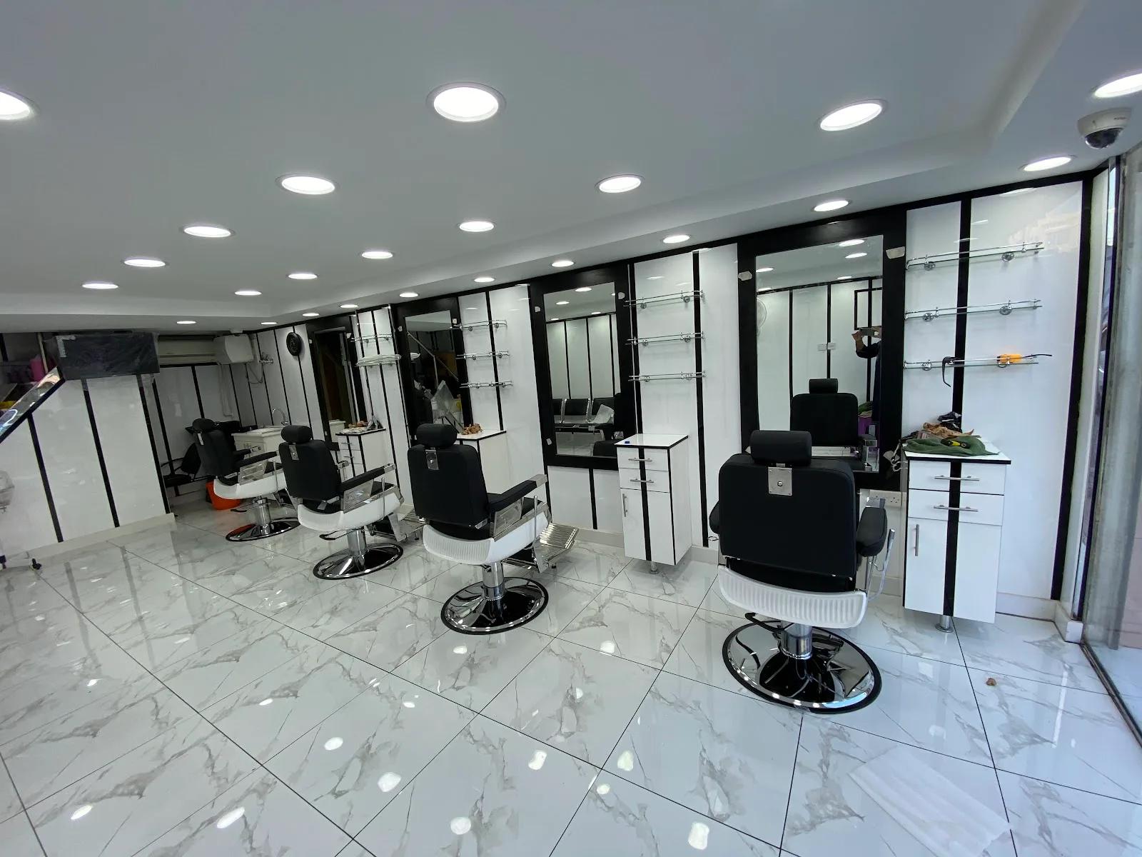 Bright, mirror-lined interior of Hair House Gents Saloon with black barber chairs and marble floor