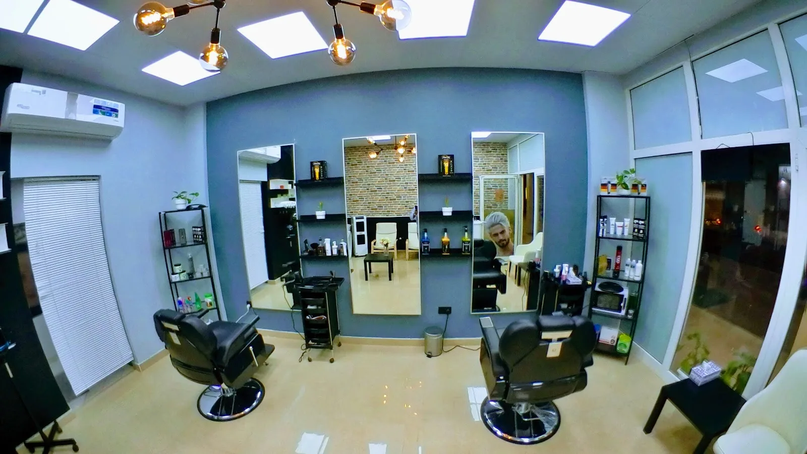 Slate-blue salon interior with two barber chairs, mirrors and brass Edison lighting