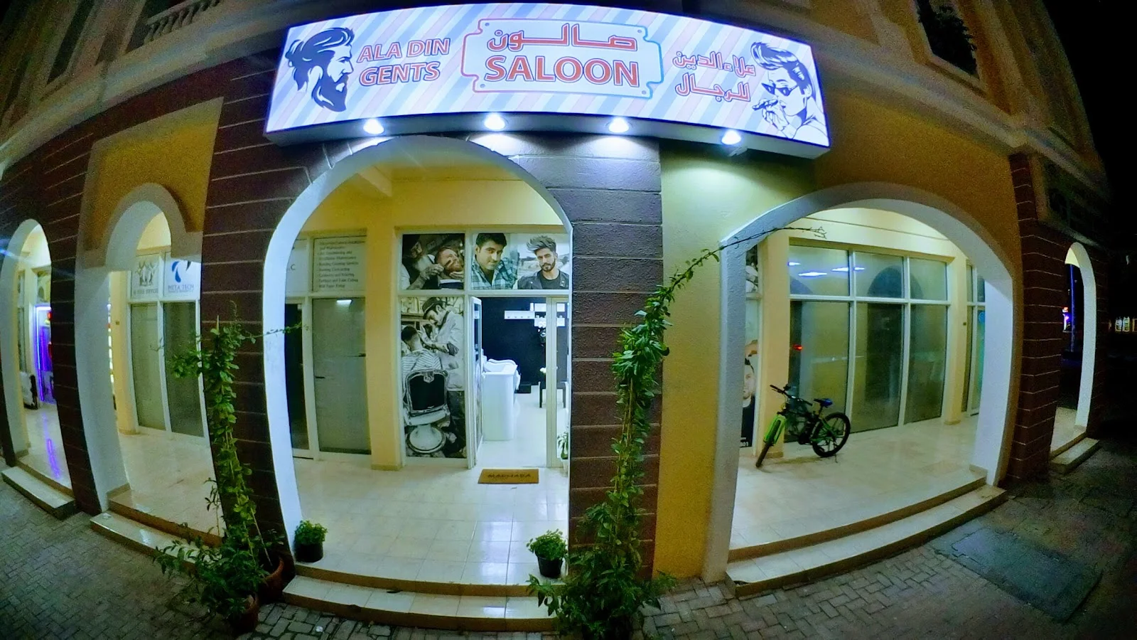 AlaDin Gents Saloon illuminated corner storefront at night in International City, Dubai