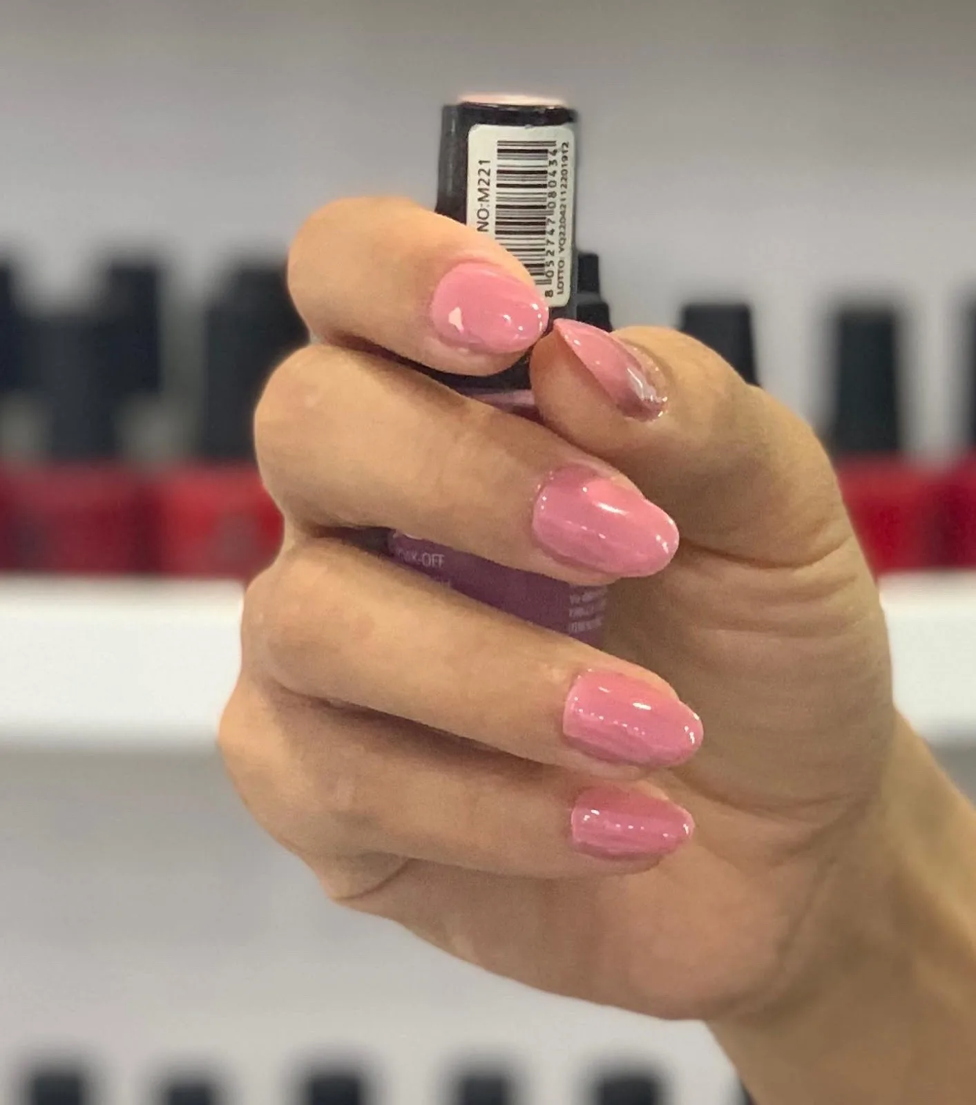 Soft pink gel manicure held beside the polish shelf
