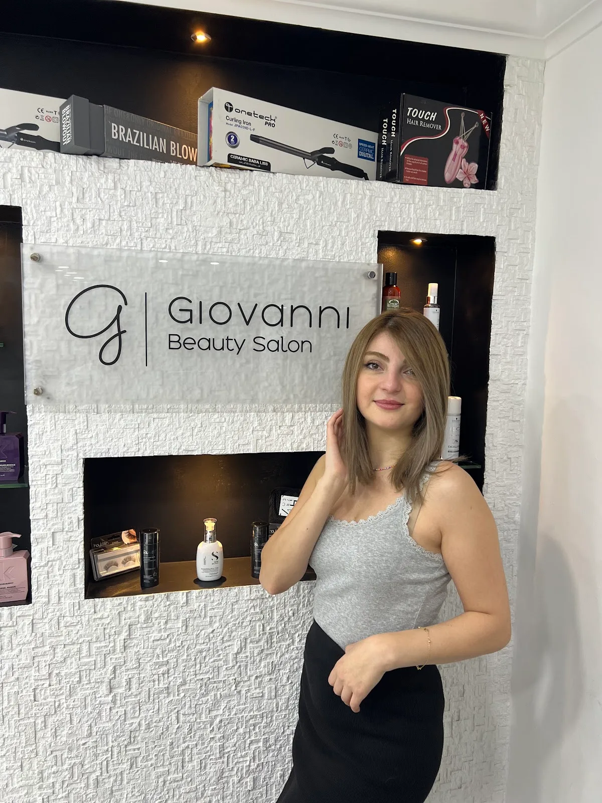 A stylist standing beside the Giovanni Beauty Salon sign and product display